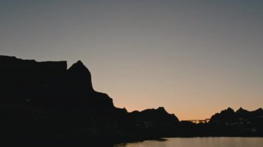 Norveç 'in Lofoten kentindeki görkemli dağ zirvelerine kurulmuş sakin bir balıkçı köyünün nefes kesici siluetini çeken geniş kapsamlı bir panoramik çekim.