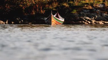 Bir kayık sakin göl üzerinde dinlenir, kayalık arazi zeminine ve yemyeşil çimenli çevreye karşı.