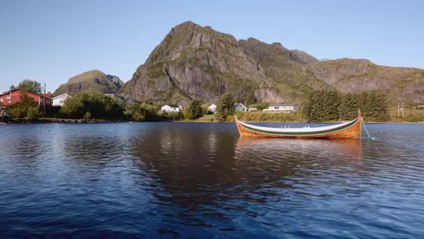 静止したロウボートをフィーチャーした静かな湖を撮影し 下の壮大なピークや家に設定し 魅力的で美しい自然の設定を作成します — ストック動画