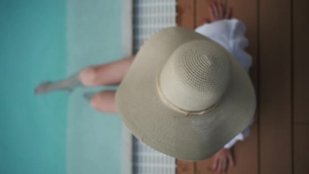 プールでリラックスした広々とした帽子をかぶった女性のオーバーヘッドショット クリスタルクリアブルーウォーターに足を浸した — ストック動画