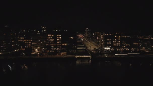 左から右にドローンパン ウォーターフロントを照らす暖かく照らされた都市の建物を明らかに — ストック動画