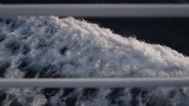 フェリーは優雅に波を貫通し 前景にぼやけた白い柵で水を飛ばす魅惑的なトレイルの後ろに残ります — ストック動画
