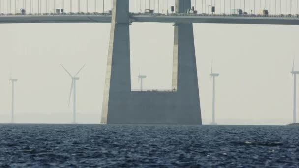 静的なショットは 回転する風力タービンのリズミカルな背景に立っているデンマークのグレートベルト橋の塔の柱をキャプチャします — ストック動画