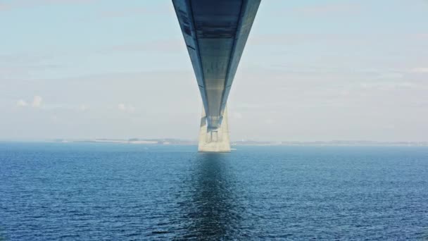 デンマークの穏やかな海に対する象徴的な構造の壮大なスパンを捉えたグレートベルト橋の下の静的なショット — ストック動画