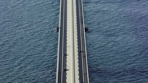 優雅に上昇する魅惑的な空中傾斜ショットは 車が遠い島に向かって象徴的なグレートベルト橋を横断するように — ストック動画