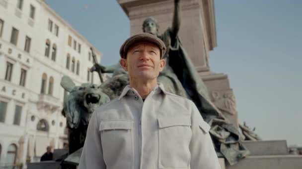 威尼斯 一个身穿夹克头戴帽子的男人欣赏圣马克狮子雕像 它是在蓝天的映衬下从一个很低的角度拍摄的 — 图库视频影像