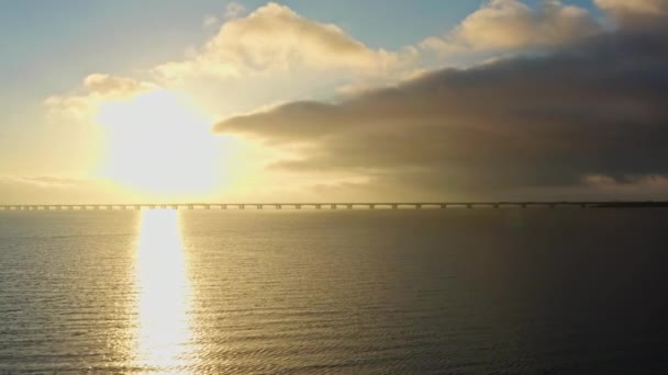 ドローンは 太陽の日の出の地平線の活気に満ちた色に優雅に沈む象徴的なグレートベルト橋を展示しています — ストック動画