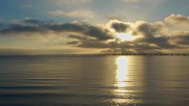 ドローンは静かな水の上を優雅に滑り 遠くにあるグレートベルト橋の絶え間ない美しさを捉えています — ストック動画