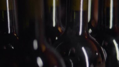 Yakın plan bir çekim, birkaç şarap şişesinin boynu ve üst kısımlarını birbirine kenetlenmiş bir şekilde yakalıyor. Parlayan ışıklar şekillerini ve detaylarını aydınlatıyor.