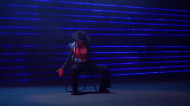 Tam bir statik çekim, yetenekli bir kadın sandalyesinin büyüleyici arka plan mavi lazer ışıklarına karşı dans edişini yakalar.