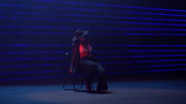 Tam bir statik çekim, canlı mavi lazer ışıklarının büyüleyici arka planına karşı sandalyede oturan bir kadın dansçıyı yakalar.