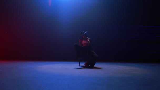 シームレスにズームアウトするハンドヘルドショット 青と赤のレーザーライトの魅惑的な光で飾られた薄暗く照らされた部屋で女性の魅惑的な椅子ダンスをキャプチャ — ストック動画