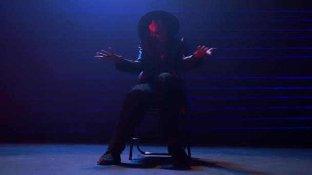 ハンドヘルドショット シームレスにズームインアウトし 鮮やかな青と赤のレーザーライトの中でチェアダンスを行う黒い帽子で女性のダンサーをキャプチャ — ストック動画