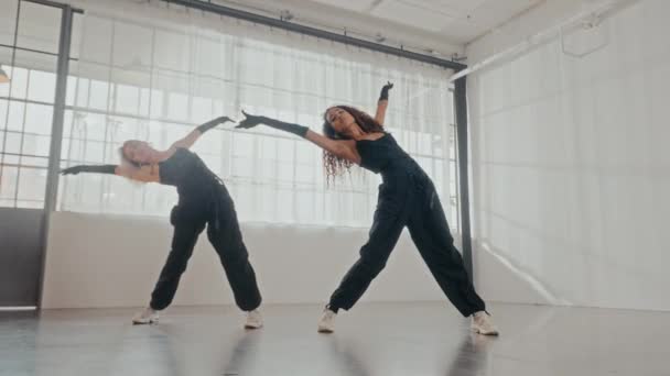 洗練された黒い服装を着た2人の女性は プロのスタジオで同期ダンスのプロレスを披露します — ストック動画
