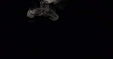 Beyaz duman izleri siyah bir arkaplanın tepesinden hareket ederek havaya karışmadan önce karmaşık desenler oluşturur.