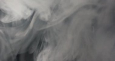 Kalın, beyaz duman havaya yükselir, siyah bir arkaplanda kaybolmadan önce girdap oluşturur.