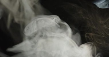 Beyaz dumandan oluşan yakın plan, karmaşık tasarımlar ve karmaşık desenler örer ve gizemli bir siyah arkaplanı aydınlatır.