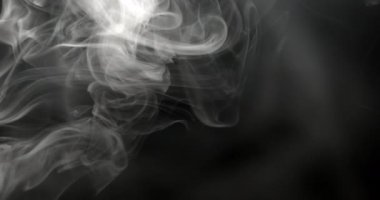 Farklı yönlerde dönen ve kıvrılan beyaz bir duman yakın plan, aydınlatma karanlık arka plana karşı dumanın kenarlarını ve hatlarını vurguluyor