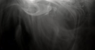 Parlak ışık, siyah zemin üzerinde dönen duman izlerini aydınlatır. Havada hareket ederken soyut desenler yaratır.
