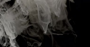 Beyaz duman izlerinin yakın çekimi yavaş yavaş siyah bir arkaplana doğru yayılıyor