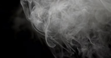 Havada parlayan beyaz duman siyah arka planda soyut desenler oluşturur.