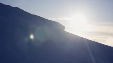 Parlak güneş, aşağıdaki karla kaplı siluetli kış manzarası üzerinde bir mercek patlaması etkisi yaratır.