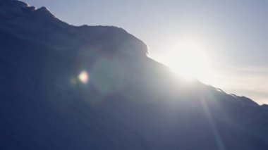 Parlak güneş ışığı, sabahın erken saatlerinde karlı yamaçlarda parlarken bir mercek parlaması etkisi yaratır.