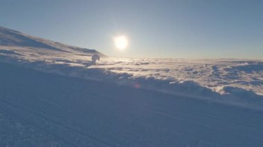 Berrak bir gökyüzünün altında sakin, karlı bir manzara. Güneş ufukta belirgindir, ışığını karlı arazide yayar.
