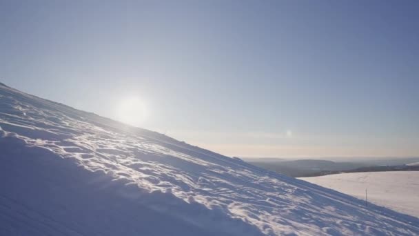 明るい太陽が地平線上に昇り 明るい空の下に広大な冬の風景の雪の斜面を照らしています — ストック動画