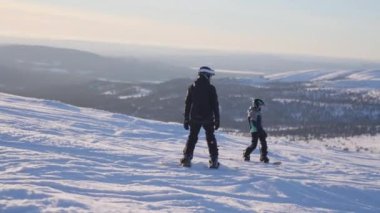 Gündüz vakti çocukların görkemli karlı arazide snowboard yaparken çekilmiş bir görüntüsü.