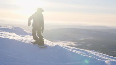 Resimli bir kış manzarası ve ışıl ışıl güneş alan arka planda snowboard yapan bir çocuğun görüntüsü.