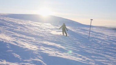 Bir iz sürme sahnesi, parlayan güneşin arka planında snowboard yapan bir çocuğu takip ediyor.