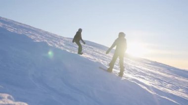 Güneşli güneşe karşı snowboardlarındaki karlı yamaçları oyan çocukların bir görüntüsü.