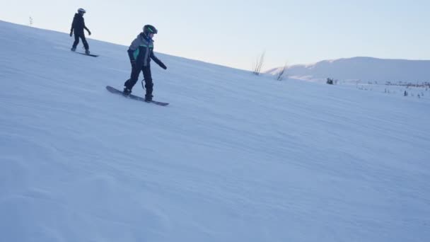 昼間の雪の斜面を介して彼らの方法を世話する若いスノーボーダーの追跡ショット ロイヤリティフリーのストック動画