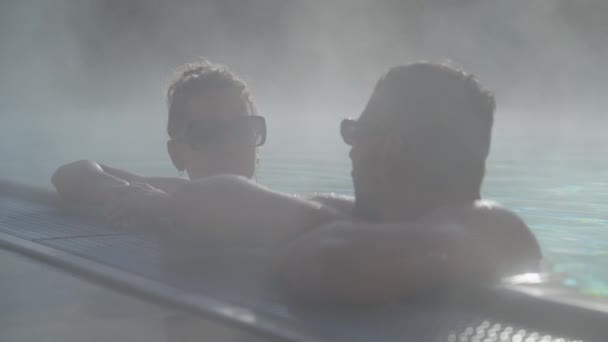 一对情侣在室外温泉浴池边聊天的特写镜头 晨光下的空气充满了薄雾 — 图库视频影像