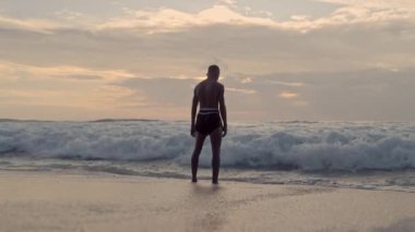 Bir Muay Thai boksörü gün batımında deniz dalgalarının gücüyle yüzleşir.