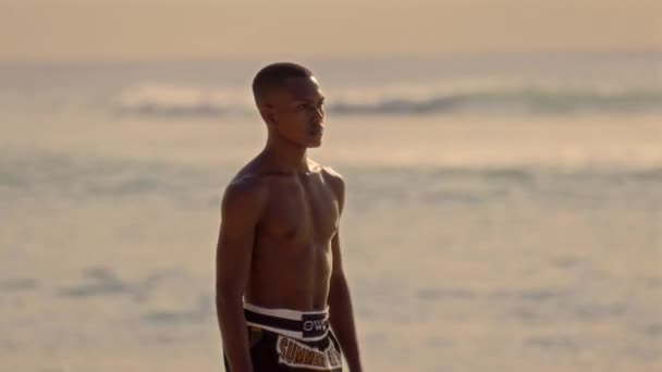 一位来自泰国的拳击手走在沙滩上 沐浴在金色的夕阳余晖中 面对着闪烁的大海 — 图库视频影像