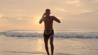 Bir Muay Thai boksörü çarpışan dalgalara ve günbatımına karşı sıkı bir eğitim veriyor.