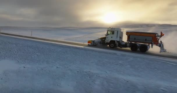 在部分多云的天空下 一架无人驾驶飞机紧跟着一辆铲雪车在冰岛大雪覆盖的道路上打扫卫生 免版税图库视频
