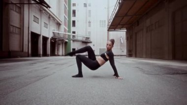 Siyah kıyafetli bir kadının, şehir sokaklarının beton kaldırımlarında çağdaş bir dans gösterisi yaparken çekilmiş yavaş çekim görüntüleri.