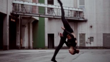 Bir kadın şehir ortamında modern dans yeteneklerini sergilerken ön takla atıyor.