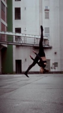 Bir kadın, çağdaş dans rutininin bir parçası olarak yavaş çekimde ön takla atarken portre yönlendirme görüntüsünde yakalanır.