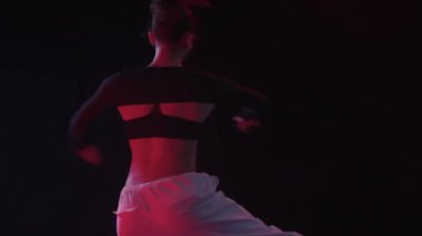 Kırmızı stüdyo ışıkları ve karanlık fon arasında zarif bir akışkanlıkla dönen genç bir kadın.