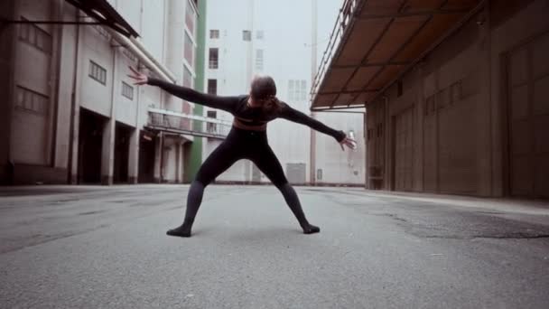 地上レベルのショットは 路地のコンクリート舗装のスローモーションで彼女のダンスルーチンを練習する熟練した都市ダンサーをキャプチャします — ストック動画