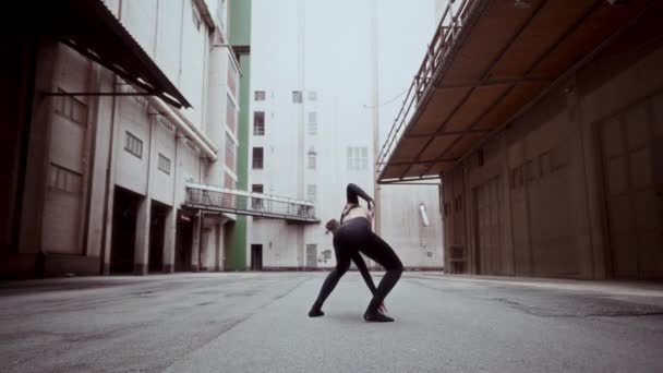 黒い服を着た女性は複雑な現代的なダンスの動きを行い 都市の路地でゆっくりとした動きでフロントフリップルーチンを実行します — ストック動画