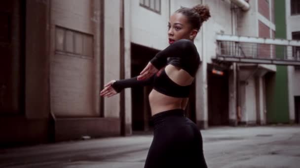 優雅なダンサーは 建物に囲まれた路地でゆっくりとした動きで表現的なモダンダンスパフォーマンスを実行します — ストック動画