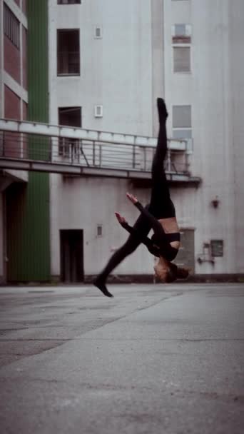 女性は 彼女の現代的なダンスルーチンの一部として ゆっくりとした動きでフロントフリップを実行しながら ポートレート向きのビューでキャプチャされます — ストック動画