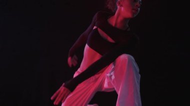Esnek genç bir kadın, her hareketini vurgulayan sıcak kırmızı ışıklarla aydınlatılmış bir stüdyoda zarifçe hareket eder.