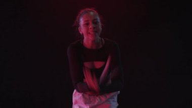 Genç bir kadın stüdyoda büyüleyici duygularla hareket eder, koyu siyah bir arka plana karşı ve ince kırmızı ışıklar ve ince duman perdeleri ile kaplanır.