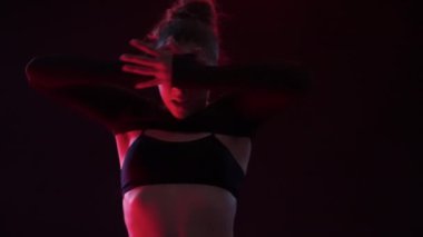 Genç bir kadın, stüdyo ışıklarının yumuşak, kıpkırmızı ışıltıları arasında zarif bir şekilde dans eder.